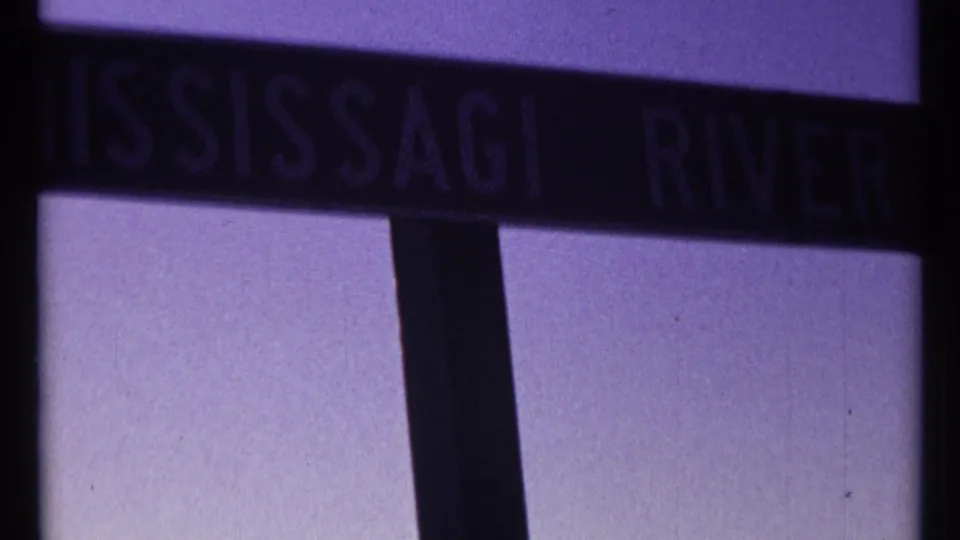 Close 1967 8mm view of a dark Mississauga River sign near Ottawa, rendered with soft focus and purple film tint.