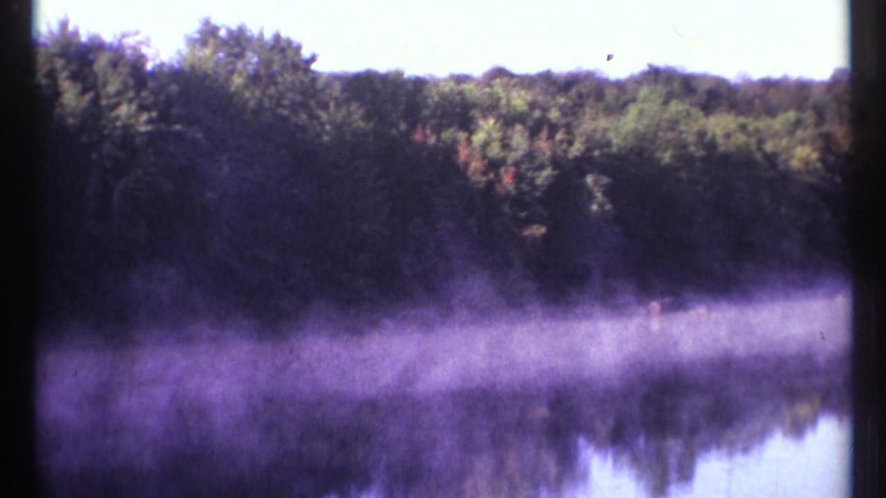 1967 Ottawa home-movie frame showing low morning fog over still lake water and a wooded far shore.