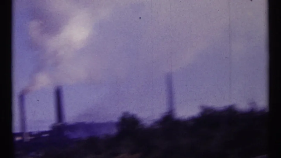 1967 Ottawa-area 8mm frame showing distant industrial smokestacks releasing smoke into a hazy sky.