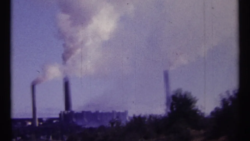 1967 Ottawa-area 8mm frame with multiple industrial stacks and drifting smoke behind foreground vegetation.