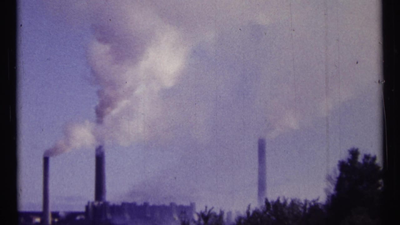 Three smokestacks release pale smoke above a distant skyline and dark trees.