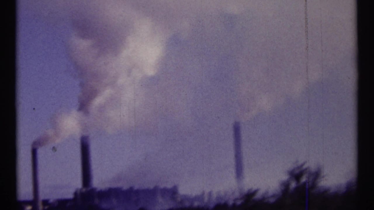 Smokestacks and drifting smoke appear across a soft, scratched film frame.