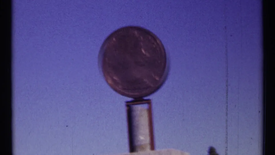 Final 1967 Ottawa 8mm frame showing the round coin display closer and softer, with blue-purple sky and film marks visible.