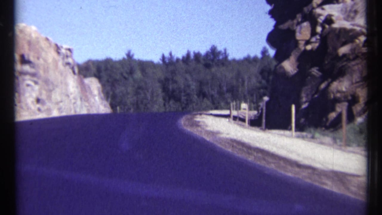 Winding paved road beside pale rock cuts and dense forest.