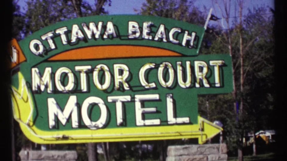 The Ottawa Beach Motor Court Motel roadside sign fills the frame, with bold white lettering, green panels, and a yellow directional arrow.