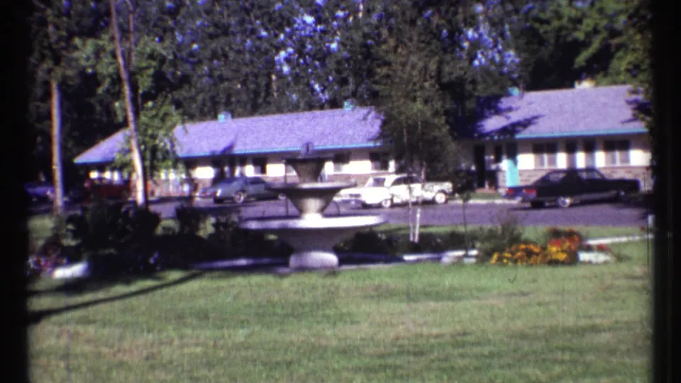 1967 Ottawa motel courtyard view with fountain, grass, trees, flowers, and mid-century cars outside the room block.