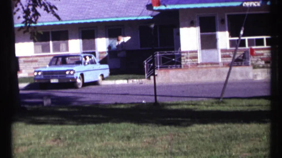 1967 Ottawa home-movie still showing a blue sedan beside a motel office, with a person at the entrance and visible roof signage.