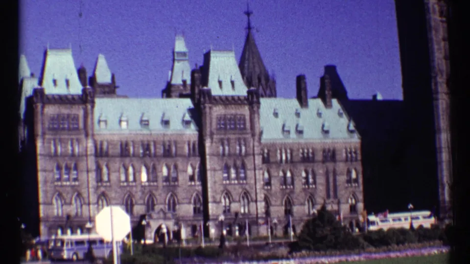 Ottawa Parliament Buildings in 1967, with Gothic Revival facade, pale roof, tower elements, small visitors, and visible 8mm frame edges.
