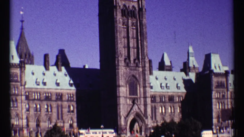 1967 Ottawa home-movie frame showing Parliament Hill architecture, including the Peace Tower, roof details, and shadowed facade areas.