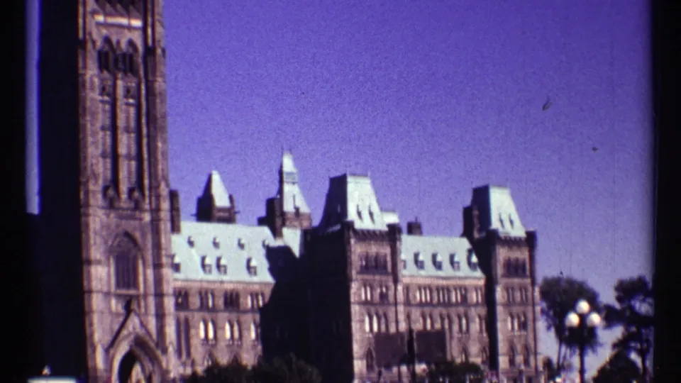 1967 Ottawa exterior view of Parliament Buildings, with Peace Tower at left, green roofs, trees, and lamps at right.