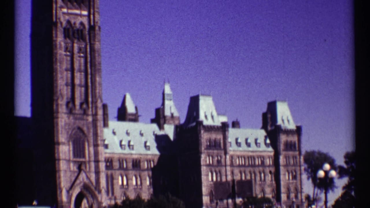 Similar view of Parliament Buildings with stone tower, rooflines, trees, and sky.