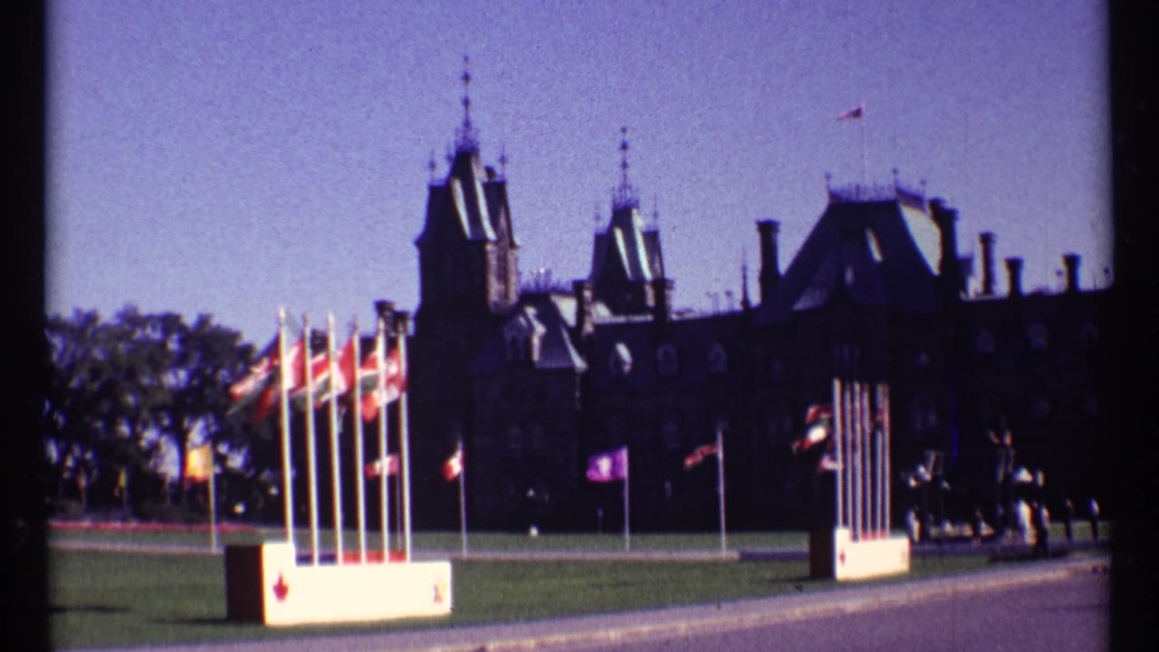 Wide view of Ottawa Parliament buildings with flagpoles on a lawn.