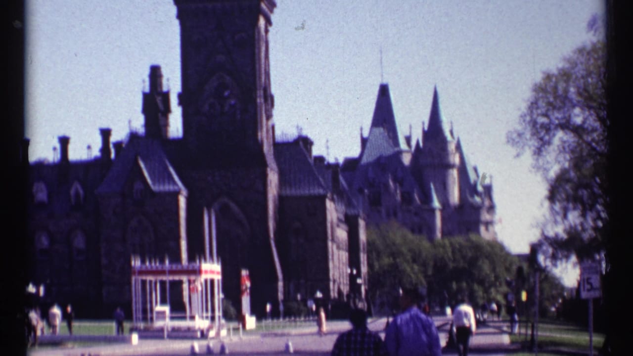 Closer view of stone Parliament buildings with pedestrians near the grounds.