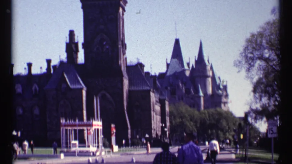 Ottawa Parliament buildings appear closer, with pedestrians on the grounds and a small striped structure near the walkway.