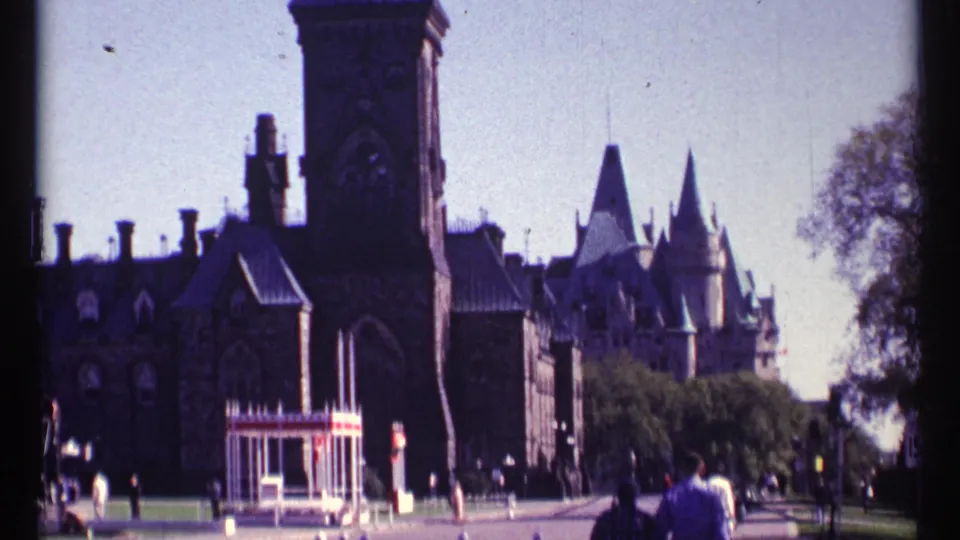 Ottawa Parliament grounds in 1967, showing Gothic Revival buildings, visitors, trees, and a roadside sign.
