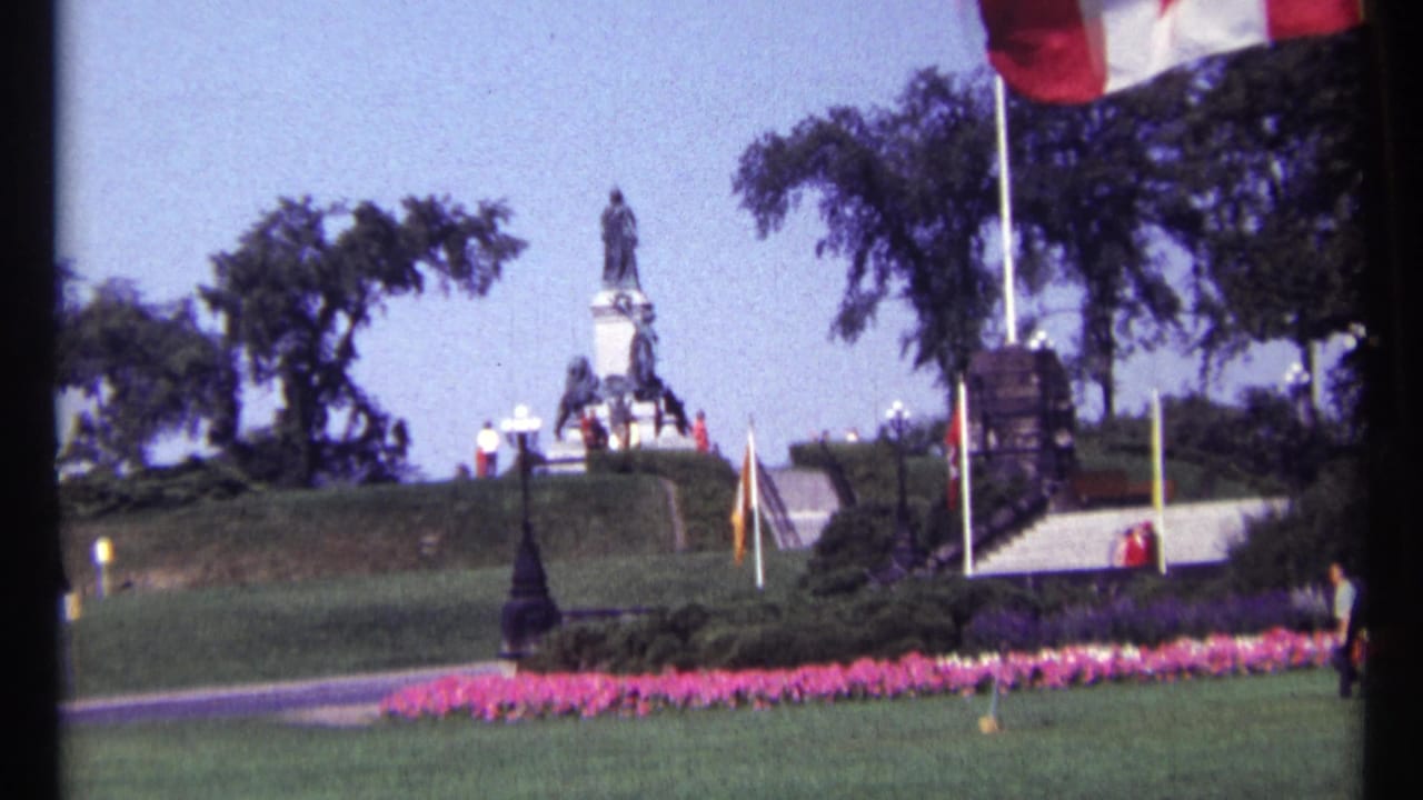 Landscaped monument grounds with a flagpole, statue, steps, lawns and visitors in the distance.