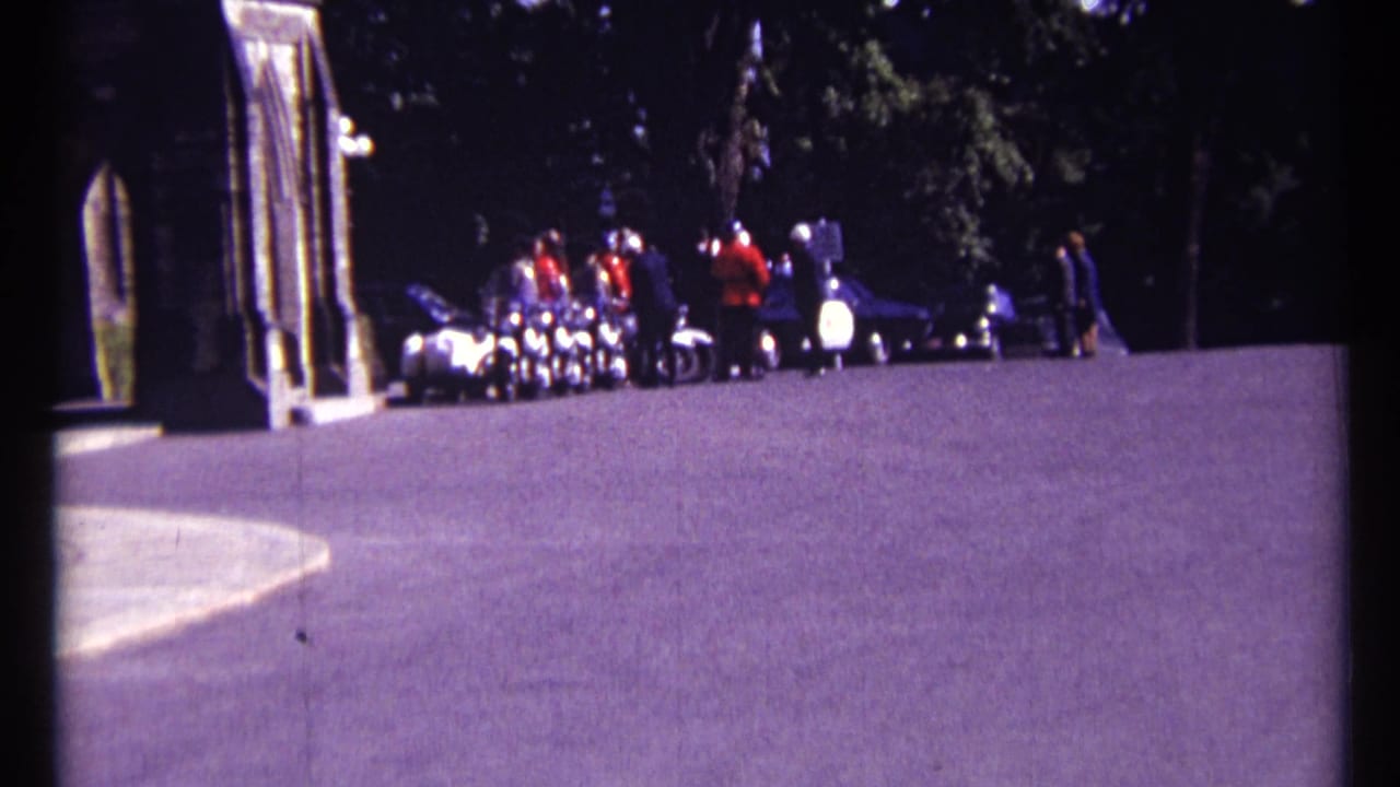 Distant RCMP officers and visitors near a stone building entrance beside a paved approach.