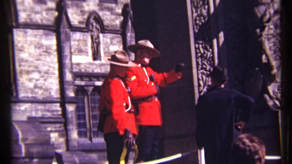 Closer 1967 Ottawa frame of two RCMP officers in red serge and hats, with one gesturing near a stone building entrance.
