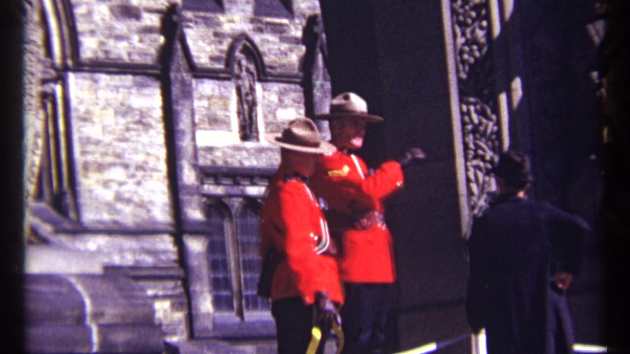 1967 Ottawa 8mm frame showing two RCMP officers in red serge outside historic stone architecture with a visitor in the foreground.