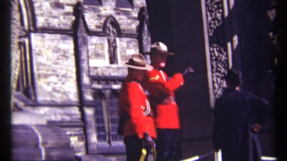 1967 Ottawa 8mm frame showing two RCMP officers in red serge outside historic stone architecture with a visitor in the foreground.
