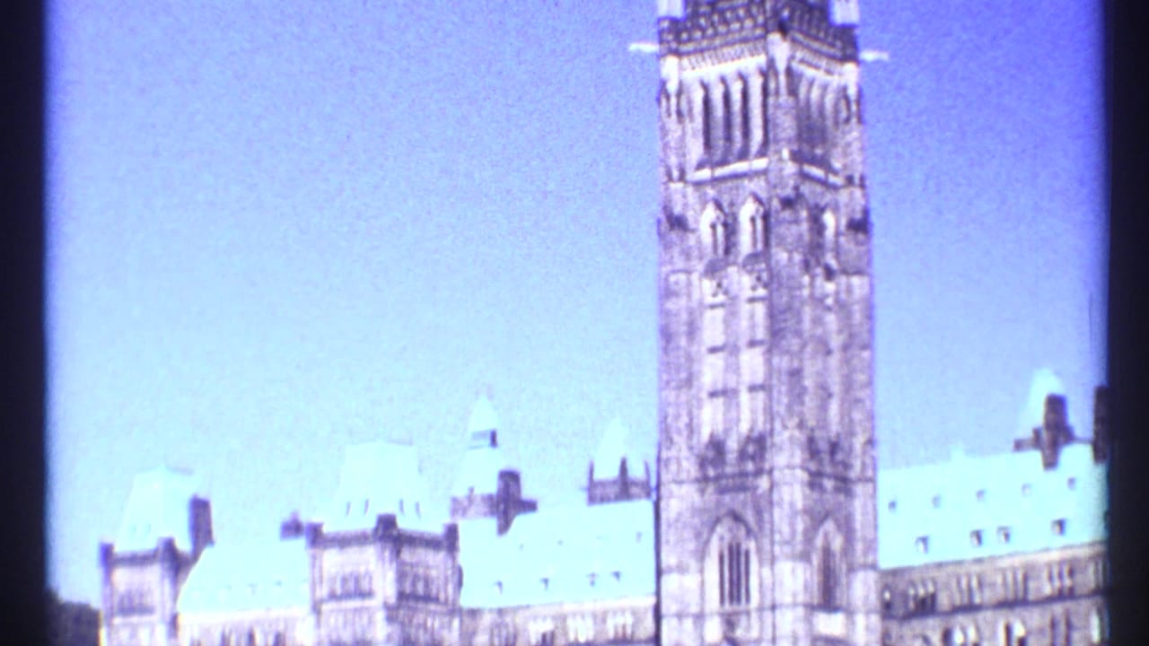 Wide view of Parliament buildings with the Peace Tower rising against blue sky.