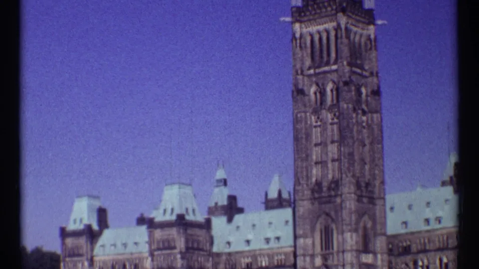 Handheld 1967 Ottawa frame with the Peace Tower rising above Parliament's roofline and blue sky.