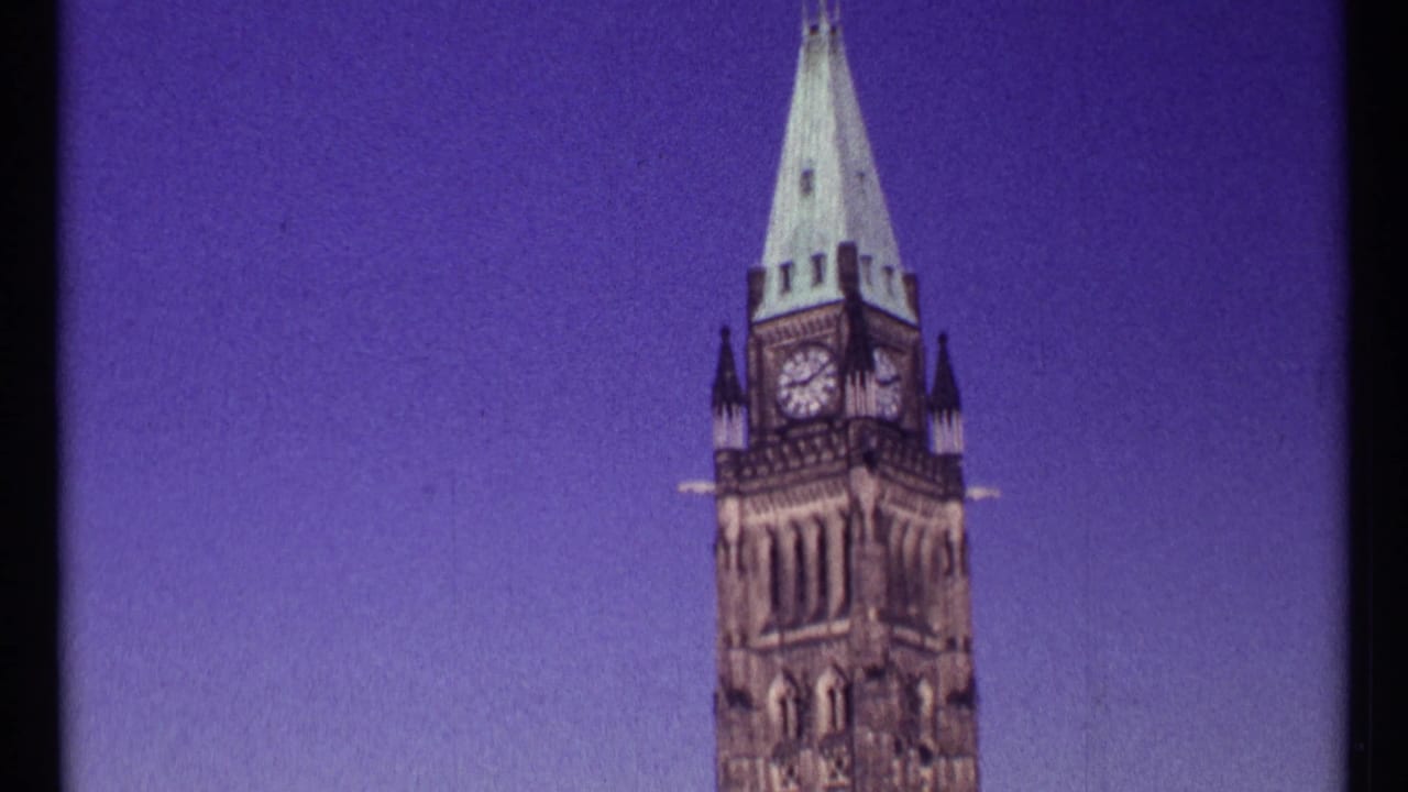 1967 Ottawa home-movie frame showing the Peace Tower clock face and spire rising against a saturated purple-blue sky.