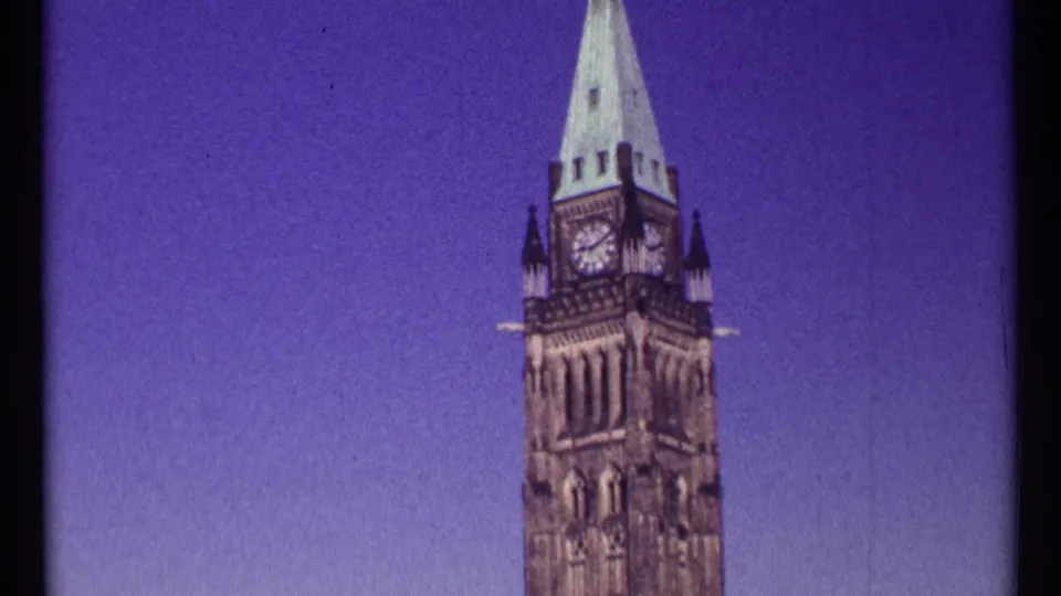 1967 Ottawa home-movie still showing a closer handheld view of the Peace Tower, with the clock face, upper stonework, and pointed roof visible.