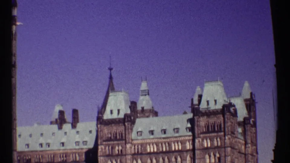 Ottawa Parliament Buildings appear in a slightly shifted 1967 8mm view, with stone towers, pale roofs, and a strong purple sky cast.