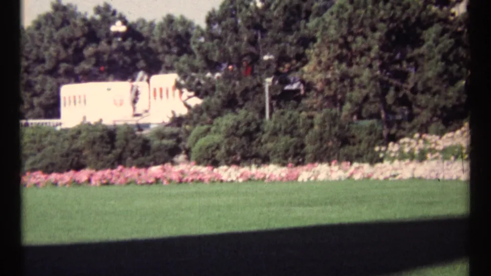 The final 1967 Ottawa frame holds on a sunlit park scene with lawn, flower beds, leafy trees, and a light-colored building in the background.