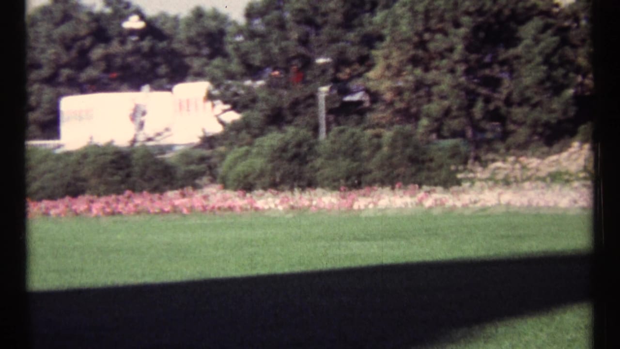 1967 Ottawa home-movie frame showing lawn, pink flowers, trees, and partial dark scan borders near a public garden setting.