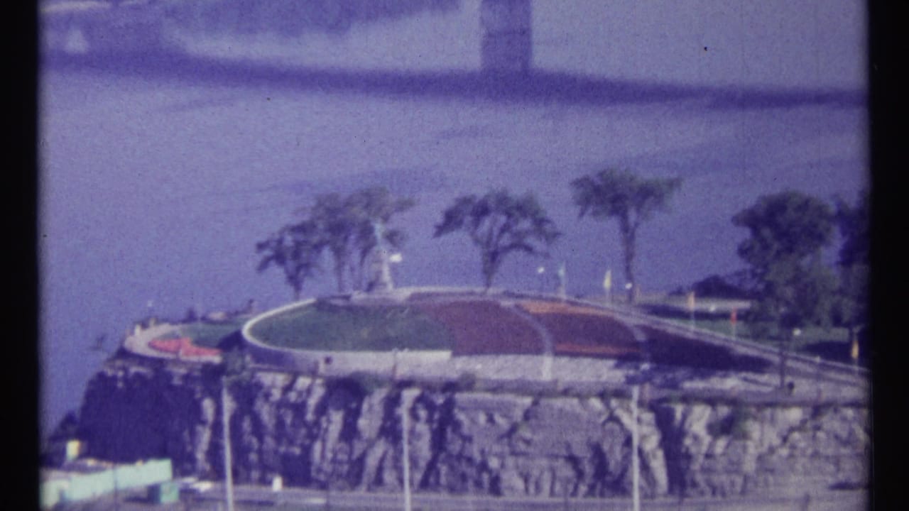 Riverfront view with landscaped cliffside park and roadway near a bridge.