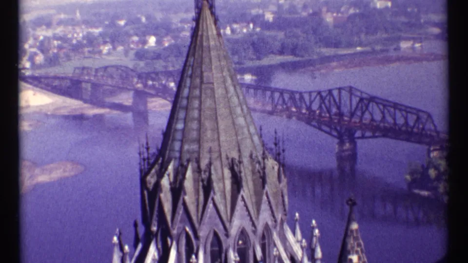 Ottawa twilight view with a Gothic spire in the foreground and a steel truss bridge crossing the river behind it.