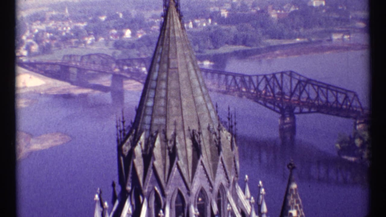 Gothic-style spire in front of a river bridge and distant Ottawa shoreline.