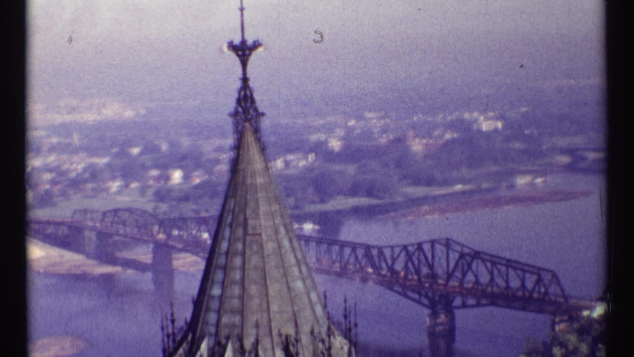 Church steeple in foreground above a river and steel truss bridge.
