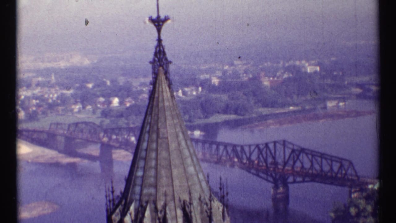 Elevated 1967 Ottawa panorama with a church steeple centered before a steel truss bridge, river, and hazy urban background.