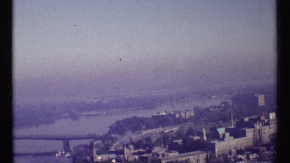 Soft 8mm Ottawa river view from an elevated position, showing riverbanks, a bridge edge, rooftops, and distant haze.