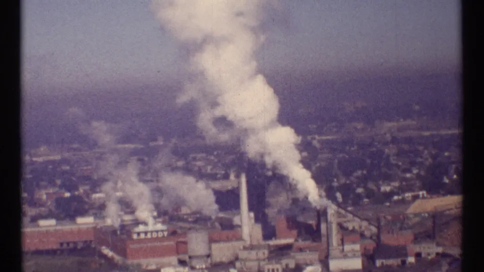 1967 Ottawa industrial view with smoke rising from several stacks, a water tower, and readable plant lettering on a building facade.
