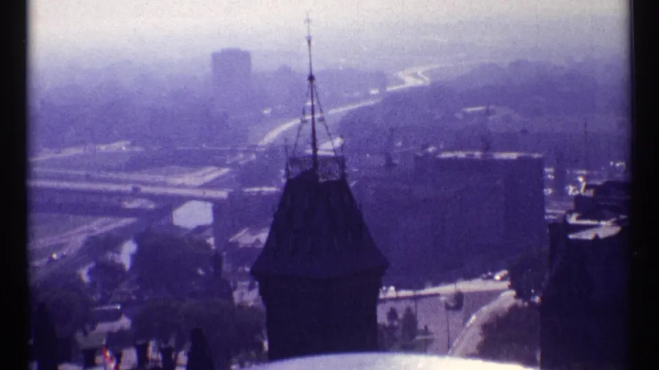 1967 Ottawa home-movie frame with a dark spire in front of hazy roads, bridge lines, and distant buildings.