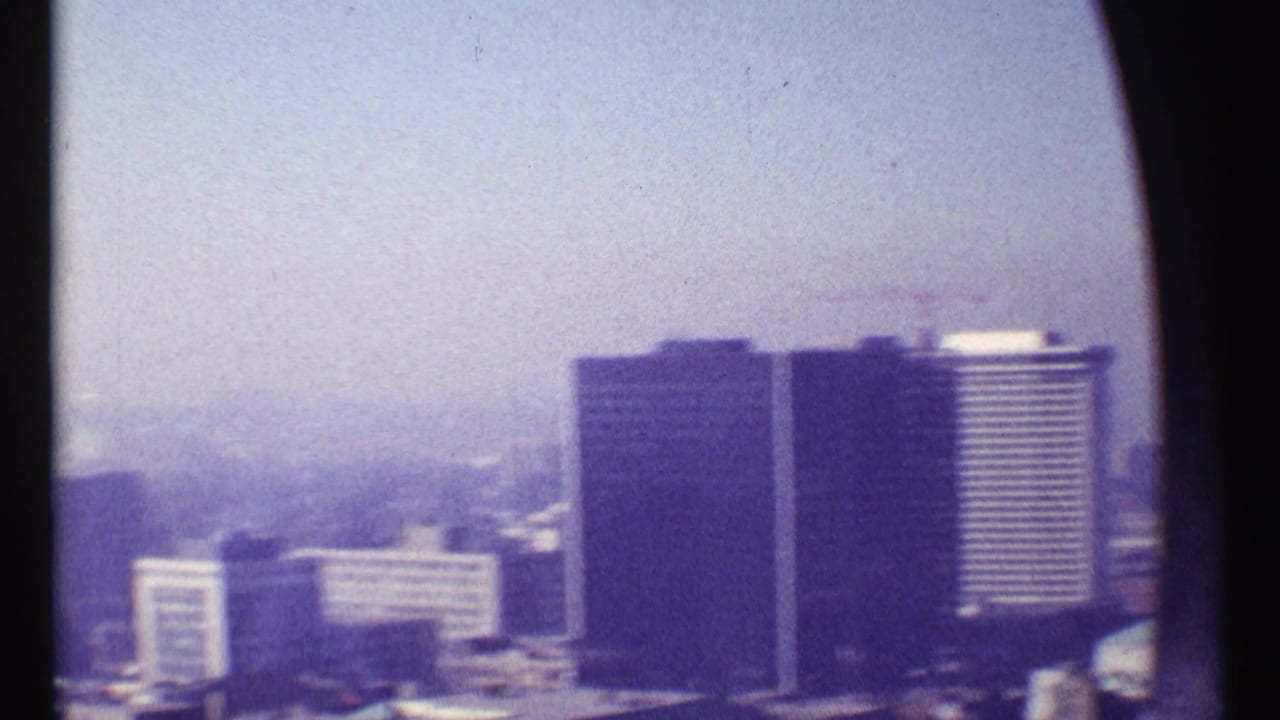 Hazy elevated view of high-rise buildings with dark frame edges and distant city skyline.