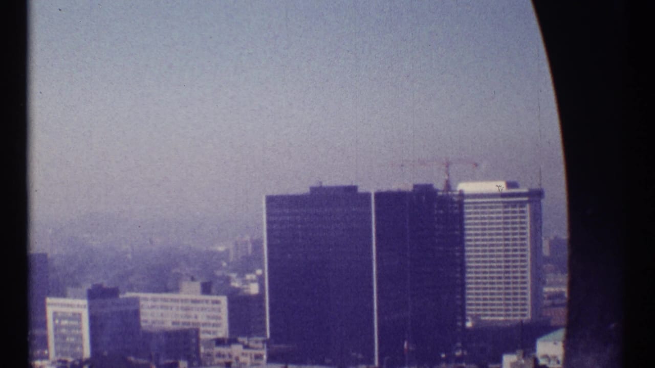 1967 Ottawa skyline view with dark modern towers, a pale gridded high-rise, and faint buildings receding into haze.