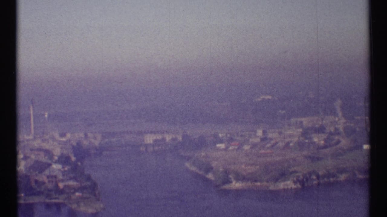 Hazy aerial view of a broad river with shoreline buildings and vertical structures.