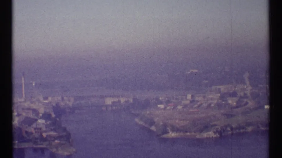 1967 Ottawa aerial view showing a broad river, developed banks, low buildings, and a hazy skyline in soft 8mm color.