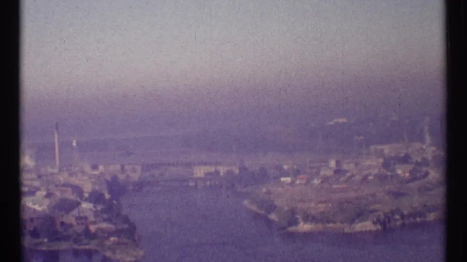 Hazy 8mm aerial view of Ottawa's riverfront, with water, landforms, shoreline structures, and distant urban features.