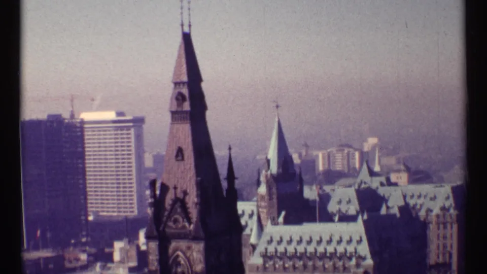 1967 Ottawa skyline view with a tall stone tower, copper-colored rooflines, modern high-rises, and distant haze.