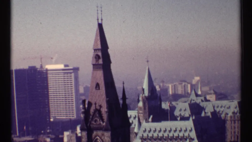 1967 Ottawa skyline frame with a dark Gothic tower in the foreground and modern city buildings beyond.