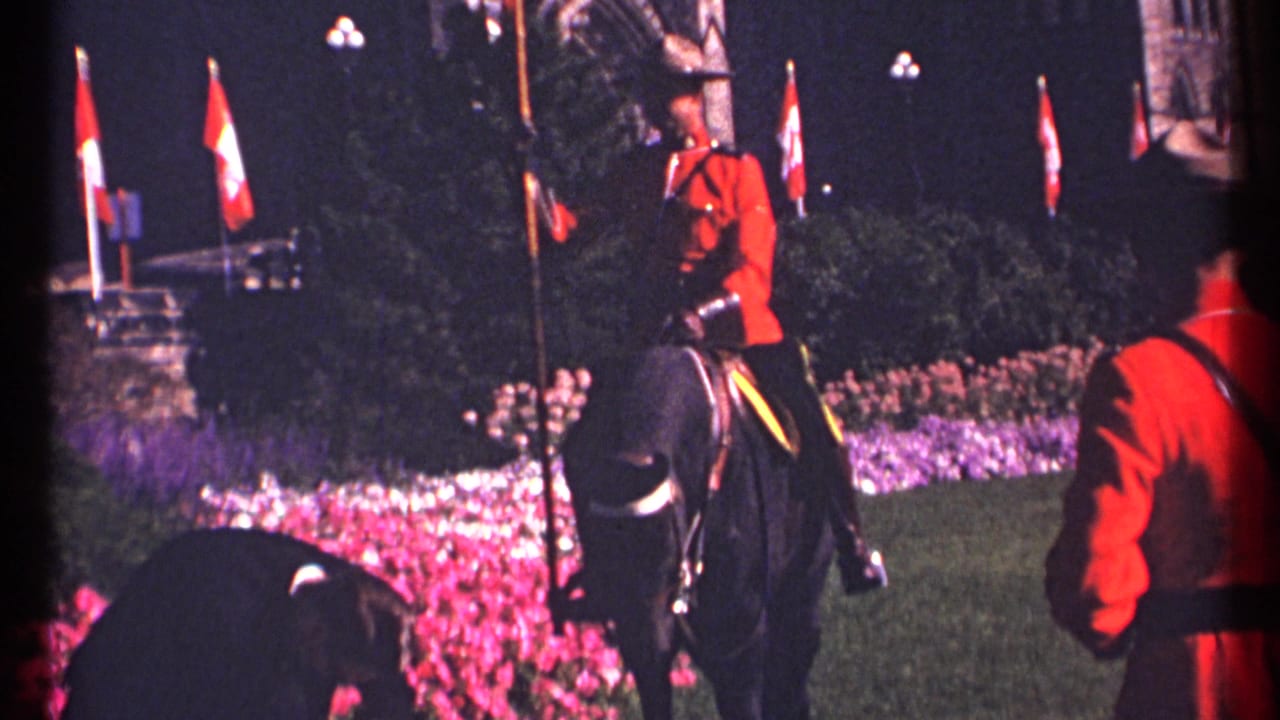 1967 Ottawa 8mm frame showing an RCMP mounted guard in red serge riding a black horse past lit flags and flowerbeds.