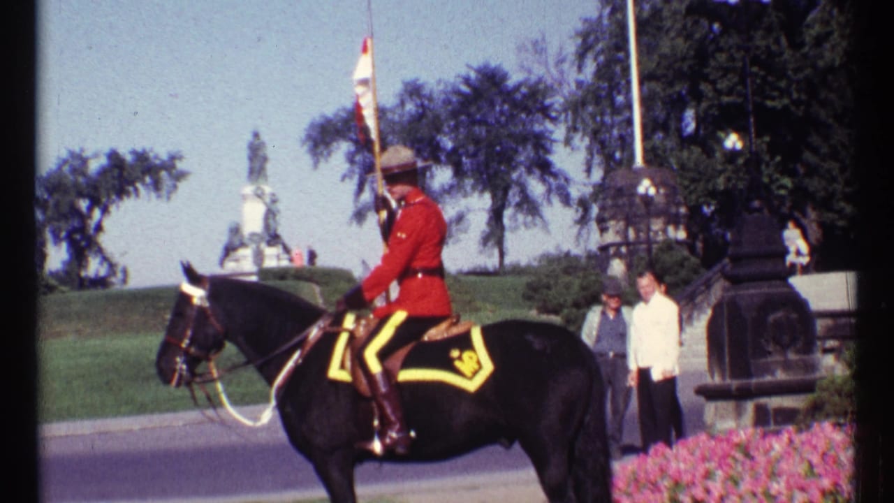 Mounted RCMP officer in red uniform on a black horse near a lawn and stone building.