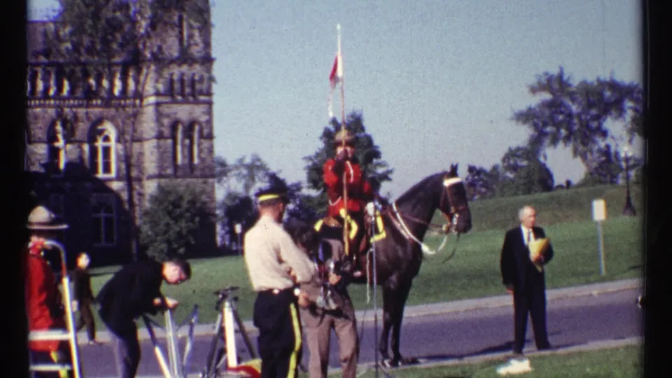 Mounted RCMP officer in Ottawa stands near a road while other personnel, tripod equipment, and onlookers occupy the ceremonial area.