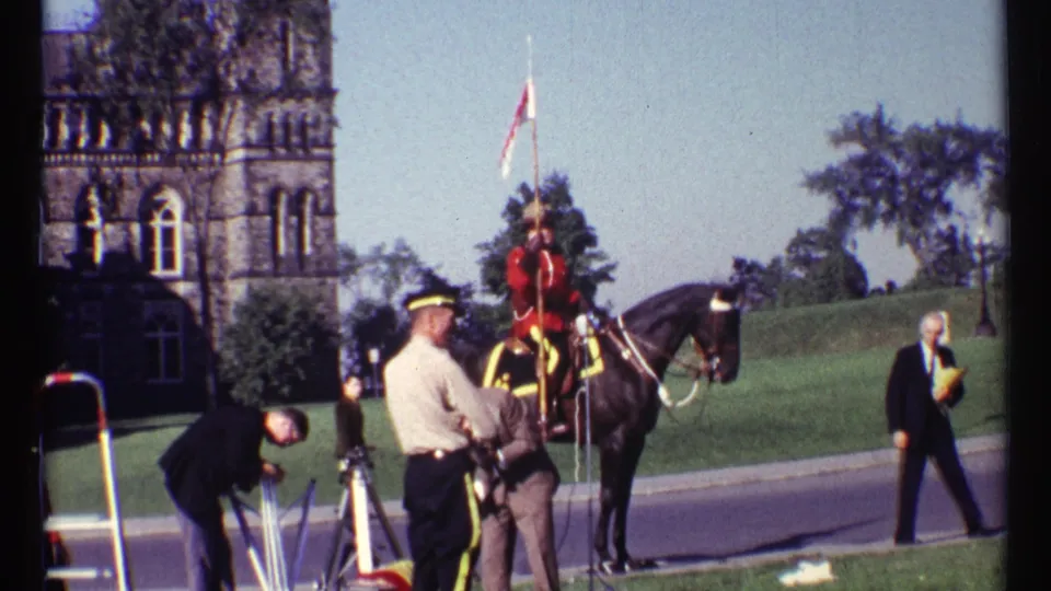 1967 Ottawa frame with a mounted RCMP officer, black horse, nearby tripod and ladder, and spectators in front of a stone tower.